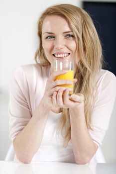 Young woman in pink shirt sitting at dining table at home with orange juice