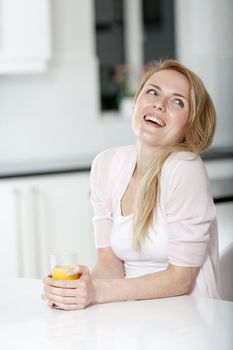 Young woman in pink shirt sitting at dining table at home with orange juice