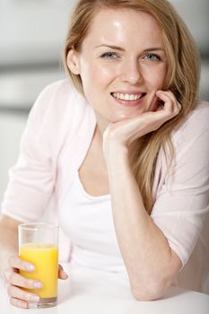 Young woman in pink shirt sitting at dining table at home with orange juice