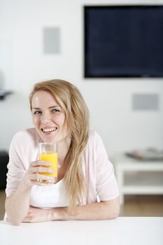 Young woman in pink shirt sitting at dining table at home with orange juice