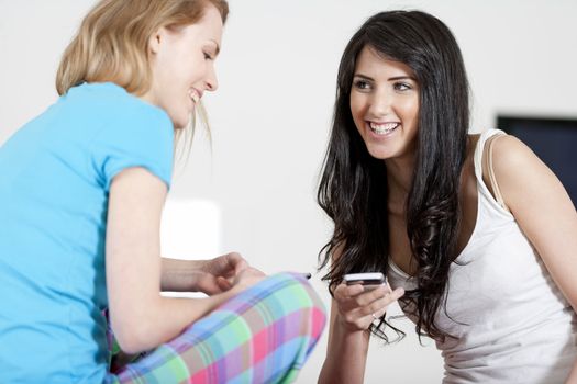 Two young woman chatting and using their mobile phones at home