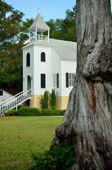 A historic two story church in Saint Marys Georgia includes a historical marker and sits behind a tree as old as the church itself