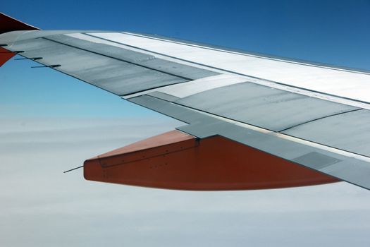 The wing of an aeroplane with orange parts in the sky