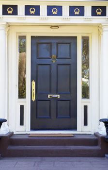 Colonial style black door on white house with  gold ornamentation above