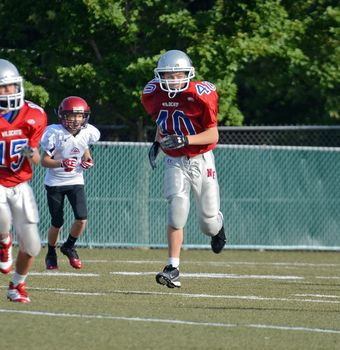 CUMMING, GA/USA - SEPTEMBER 8: Andy Leggett running to make a play with 2 unidentified opponents during a football game. Two teams of 7th grade boys September 8, 2012 in Cumming GA. The Wildcats  vs The Mustangs.