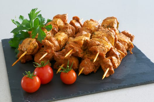 Meat brochettes on a black slate tray with some tomatoes and parsley