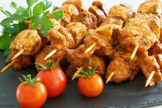 Meat brochettes on a black slate tray with some tomatoes and parsley