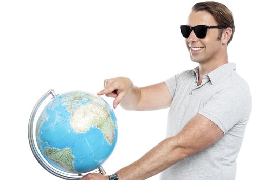 Handsome guy in goggles pointing at globe. Isolated on white background
