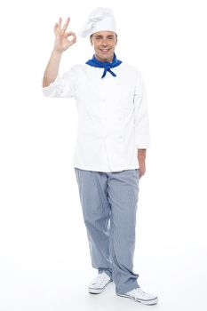 Full length portrait of chef showing okay sign to camera isolated over white