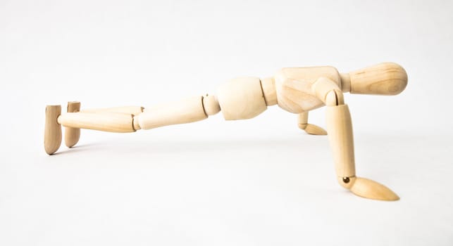 Wooden mannequin doing push-ups on white background