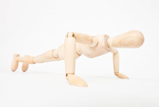 Wooden mannequin doing push-ups on white background