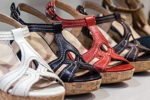 A row of colorful  leather feminine sandals on a shelf of a shoes store.