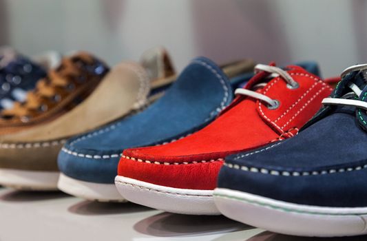 A row of colorful  summer masculine shoes on a shelf of a shoes store.Selective focus on the red one.