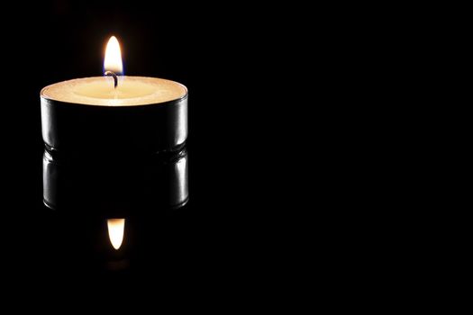 one burning tea candle on black reflective background