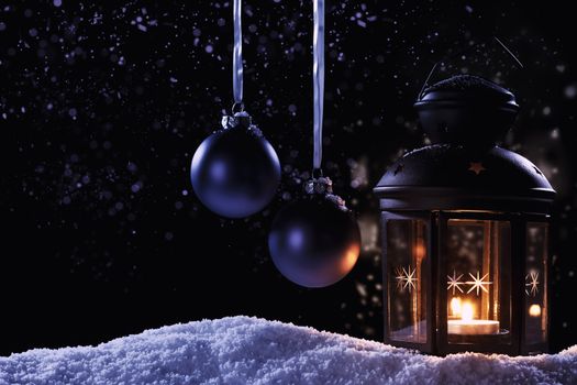 burning lantern at night  with two hanging blue christmas balls in snow at night