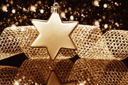 christmas ball in star shape in front of a metal ribbon and sparkling golden black background