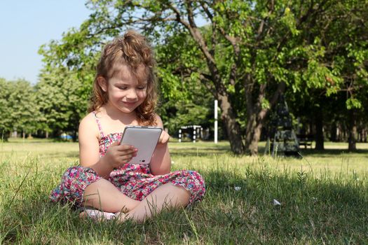 little girl sitting on grass and play with tablet pc