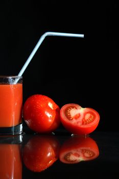 Glass of tomato juice near tomatoes on black background