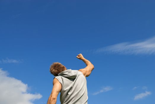 Sporty young man with his arm raised in joy, on blue sky background.