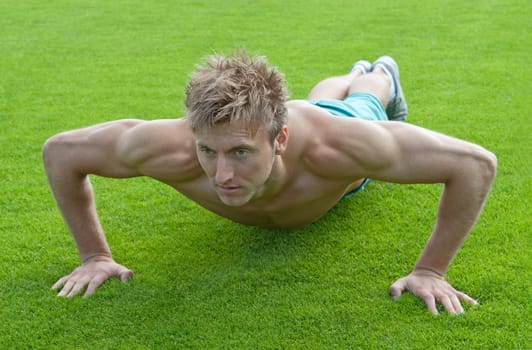 Young man training outdoors and doing push-ups on green grass.