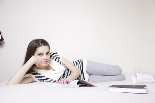 Young woman in bed rearding a fashion magazine