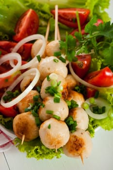 Asian pork or chicken fried meatballs with salad tomatoes and onion on white plate and white background.