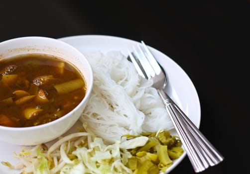 Tai curry noodles with vegetables on a white plate.