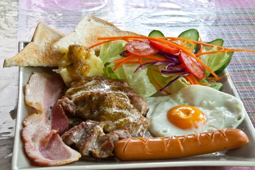 Steak pork, bacon, fried egg, sausage, bread and salad.