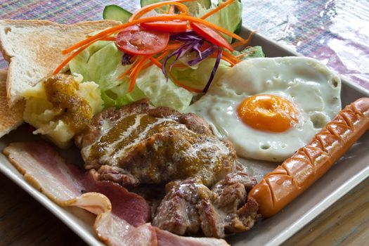 Steak pork, bacon, fried egg, sausage, bread and salad.