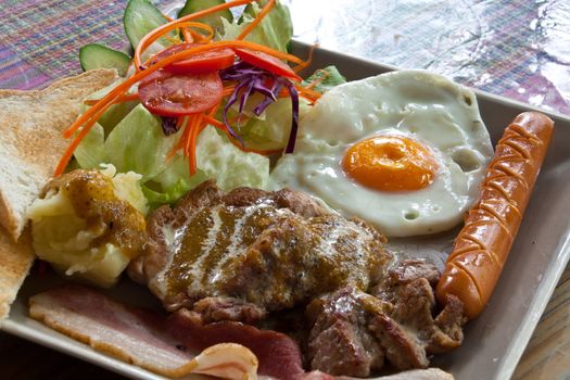 Steak pork, bacon, fried egg, sausage, bread and salad.