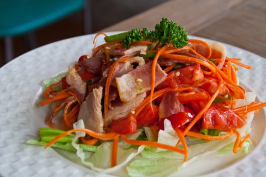 Spicy bacon salad with tomato carrot on white dish.