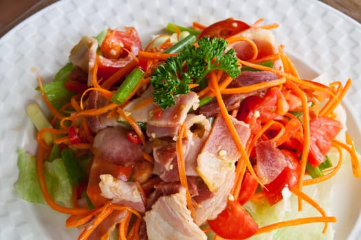 Spicy bacon salad with tomato carrot on white dish.