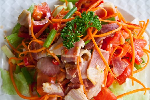 Spicy bacon salad with tomato carrot on white dish.