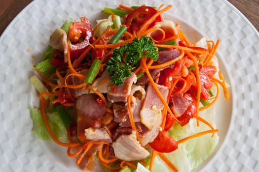 Spicy bacon salad with tomato carrot on white dish.