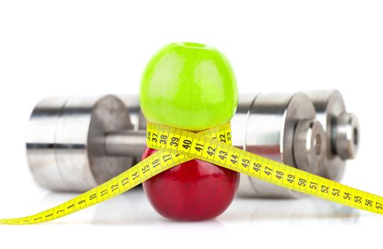 Photo of green and red apple tied with measuring tape on the background of metallic dumbbells