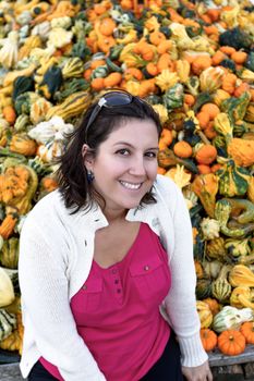 Woman infront of diffrent colors of ornamental pumpkins with fall clothings.