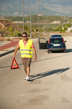 Male walking with a triangle to secure his broken down car