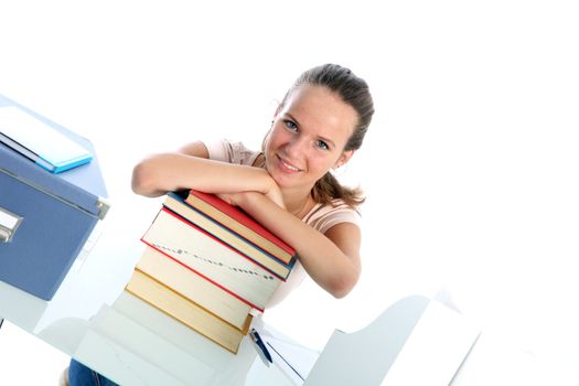Smiling confident student sitting at her desk leaning on a tall stack of textbooks, angled view against white 