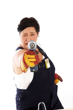Playful woman in dungarees and apron taking aim with a handheld electric power drill as she has fun during a DIY project 