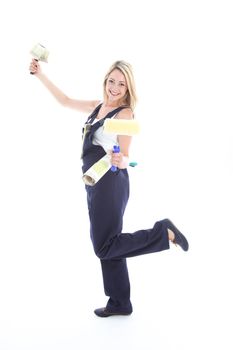 Joyful DIY woman decorator in dungarees posing playfully on one foot with a roll of wallpaper and brushes Joyful DIY woman decorator in dungarees posingplayfully on one foot with a roll of wallpaper and brushes 