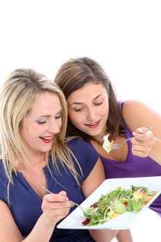 Two attractive young female dieters sharing a fresh green leafy salad eating off the same plate as they keep on eye on one another in friendly comraderie 