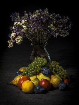 Organic fruits and vegetables on dark background with flowers
