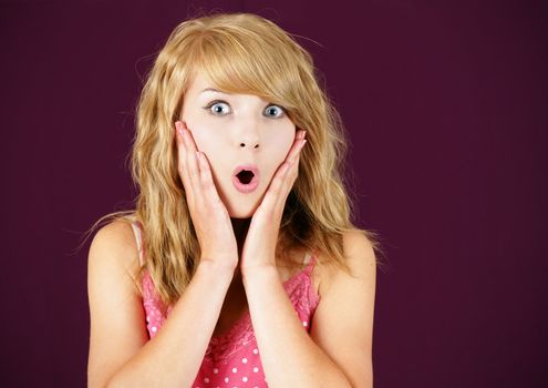 Portrait of a surprised pretty young blond girl teenager or woman over purple background