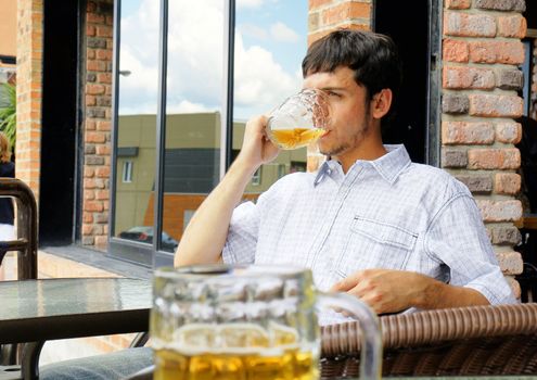 Young man or student drinking beer from glass bock while sitting outside at pub or restaurant terrace. 