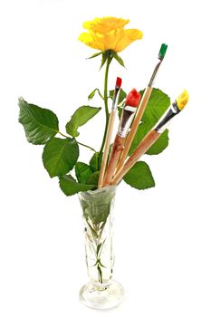 Rose and paintbrushes in glass vase against white background