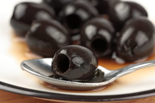 Black olive on spoon on background heap of black olives blurred