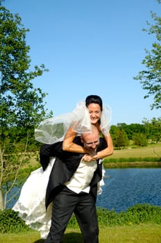 Groom is lifting his bride up in a park.