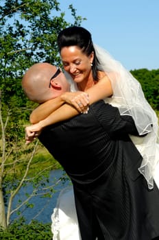 Groom is lifting his bride up in a park.