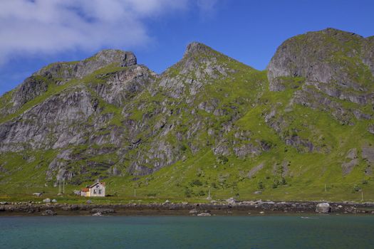 Old abandoned house by fjord surrounded by tall mountain peaks on Lofoten islands, Norway