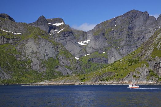 Scenic norwegian fjord, Reinefjorden, on Lofoten islands, Norway, with small fishing boat passing by